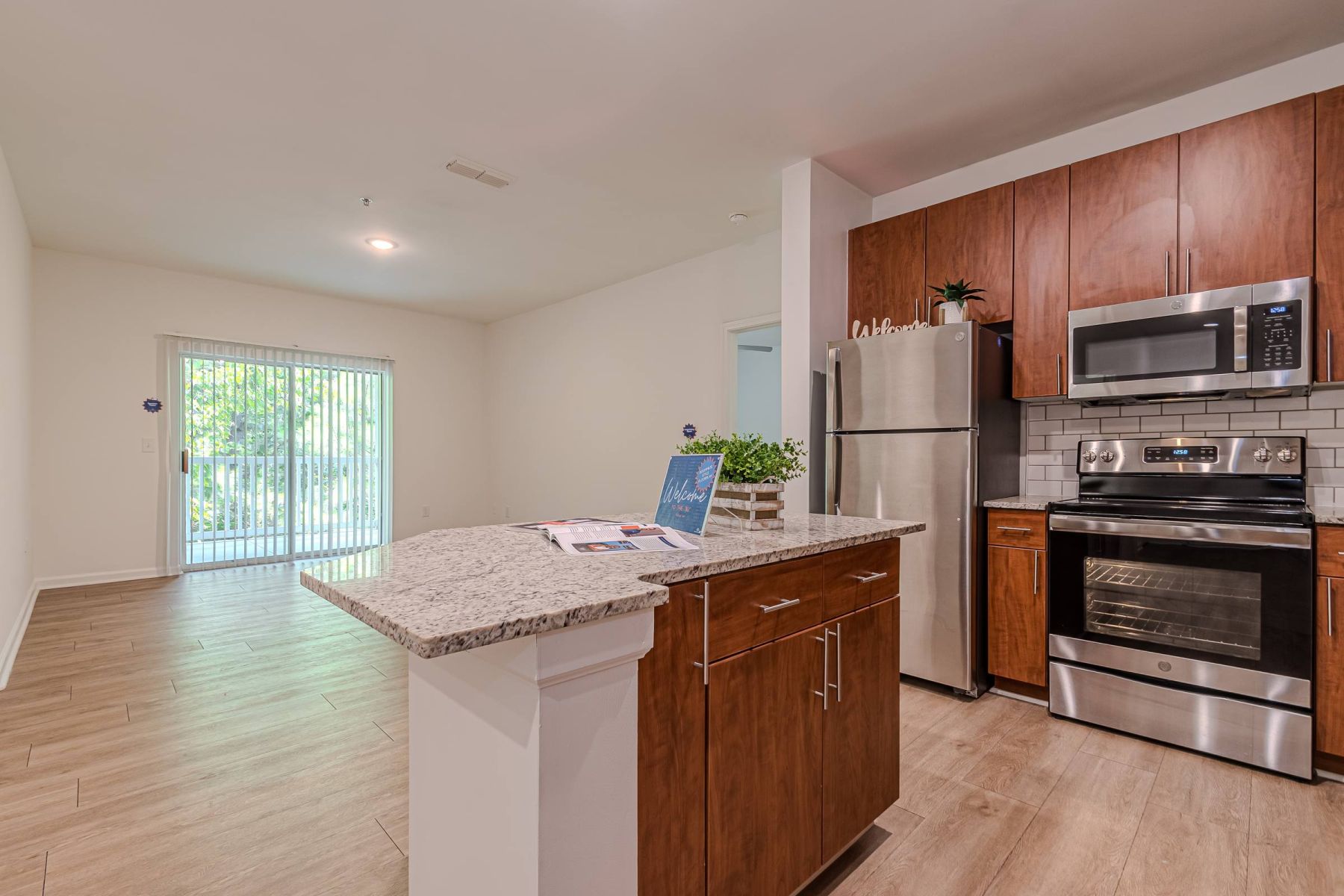 Empty room with wood floors, ceiling fan, and sliding glass door leading to a patio with vertical blinds at Apex West Midown.